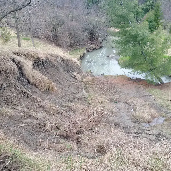 A steep hill with exposed soil and landslide damage leads to a creek