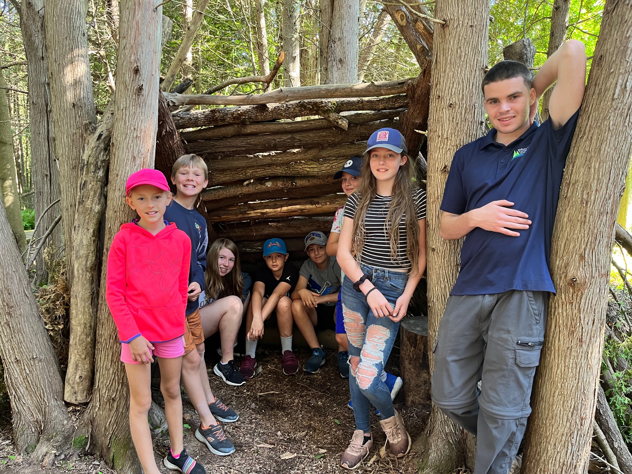 Children at Baxter building outdoor forts with tree branches with their instructor.